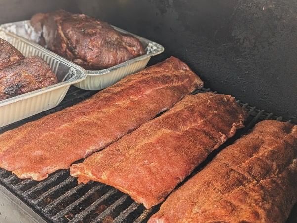 Racks of ribs coated in Spice Beautiful rub on the smoker grate, with pork butts behind them